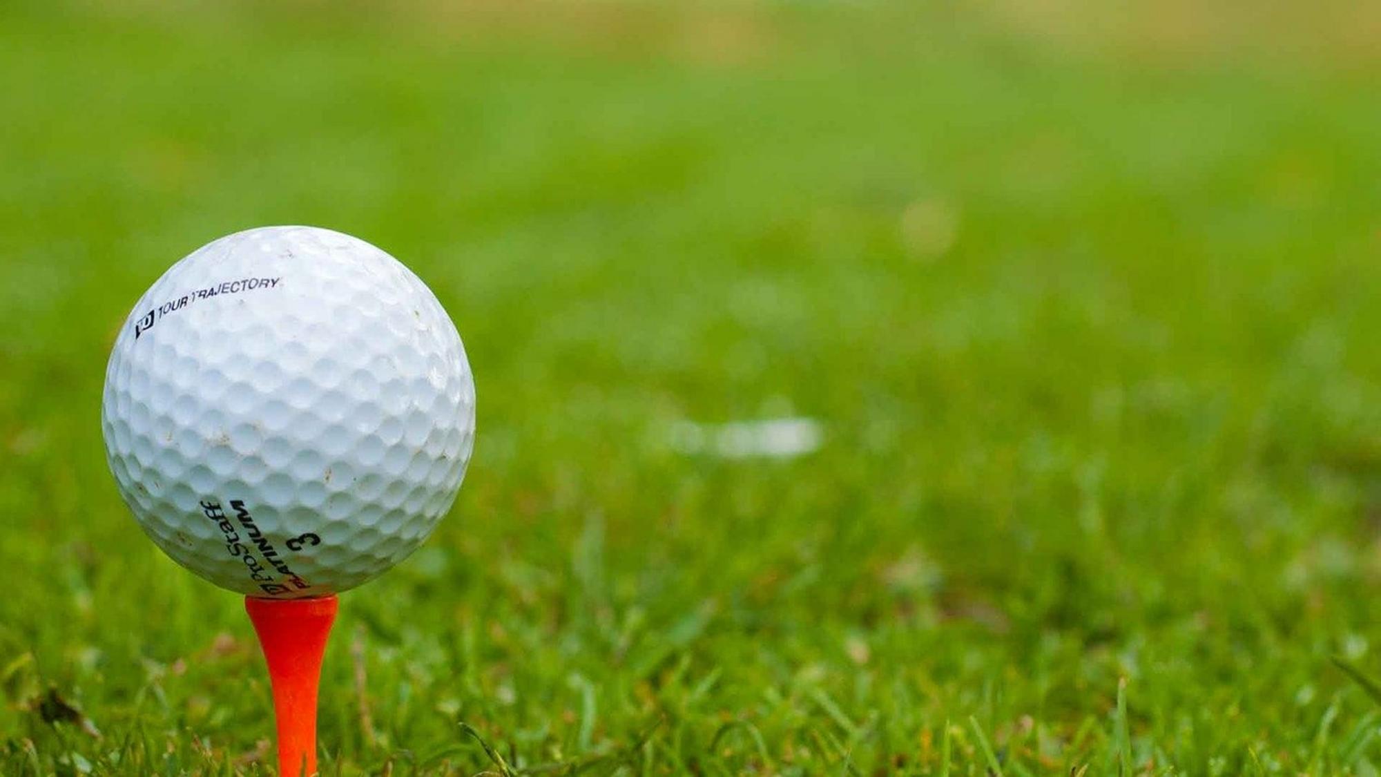 Nahaufnahme eines weißen Golfballs auf orangefarbenem Tee, platziert auf grünem Rasen – typisches Golfsport-Motiv.