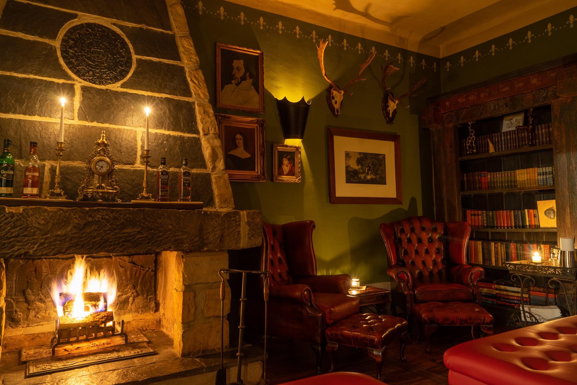 Gemütlicher Raum mit Kaminfeuer, Holzverkleidung, Bücherregal, Sessel und Beistelltisch – rustikales Ambiente im Schloss Milkersdorf.