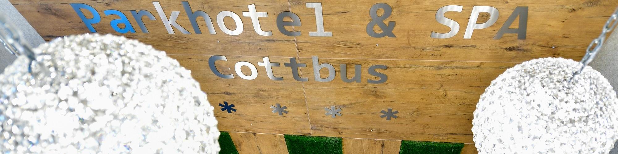 Draufsicht auf die Hotellobby mit weißen Kronleuchtern und Holzvertäfelung an der Wand mit dem Hotelnamen drauf.